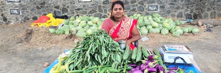 A woman sits in front of a large pile of vegetables.